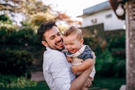 Joyful father holding his baby outdoors in a sunny garden, sharing a moment of laughter and love.